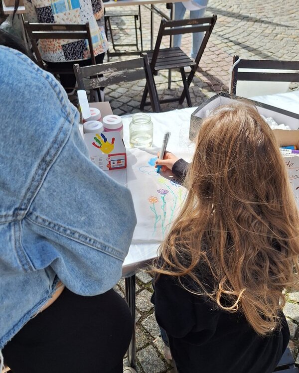 Mit Herz und Kreativität dabei Ein Kind malt mit bunten Stiften Blumen auf ein Blatt Papier bei der Bastelstation der Euro Akademie. Daneben stehen Gläser mit Wasserfarben und weitere Bastelmaterialien. Die Aktion findet im Rahmen des Frühlingsfests statt.