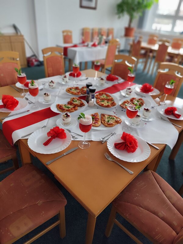Praxisnahe Berufsorientierung: BRAFO im Strukturelement I Ein festlich gedeckter Tisch mit Herz-Pizzen, roten Servietten in Blumenform und dekorativen Getränken. Die Farbkombination aus Rot und Weiß verleiht dem Tisch eine elegante und romantische Atmosphäre.