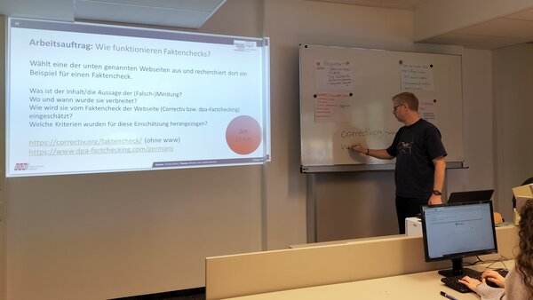 Jugendliche werden zu Faktencheckern! Auf die Wand vorne in einem Klassenzimmer wird ein Bild mit Verhaltenspunkten bei Fake News projiziert.