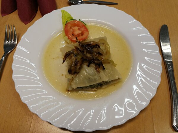 BRAFO-Projekt: Kreative Küche bringt Vielfalt auf den Tisch Auf einem Teller befindet sich eine große Maultasche mit angebratenen Zwiebeln darauf.