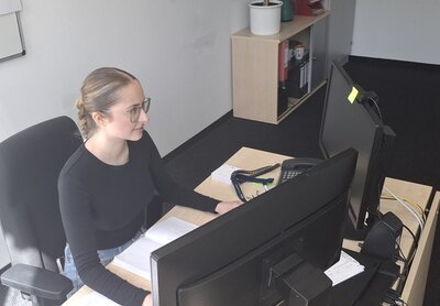 Auszubildende Auszubildende der Euro-Schulen und der Euro Akademie Berlin, Chiara Postaru, sitzt an einem Schreibtisch vor dem Computerbildschirm, sie trägt ein dunkles Oberteil, eine Brille und die Haare zusammengebunden zu einem Zopf.