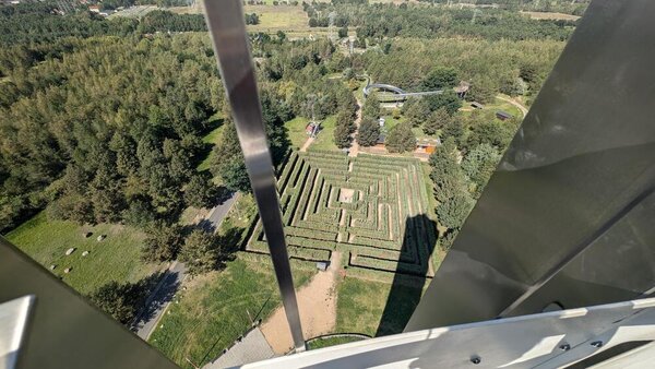 Abschlussfahrt: Erlebnispark Teichland Der Blick zeigt von einem hohen Turm durch ein Metallgitter auf den darunter liegenden Irrgarten sowie eine Sommerrodelbahn. Außen herum sind Wiesen und Wälder.