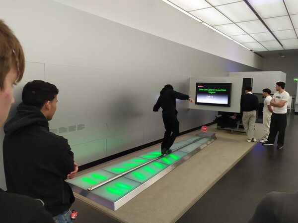 Sonniger Exkursionstag der Euro-Schulen Dresden: Spannende Einblicke in Wissenschaft und Kultur Eine Person testet ihre Reflexe auf einer beleuchteten Laufbahn in einem Technik- oder Wissenschaftsmuseum. Andere Personen beobachten das Experiment.