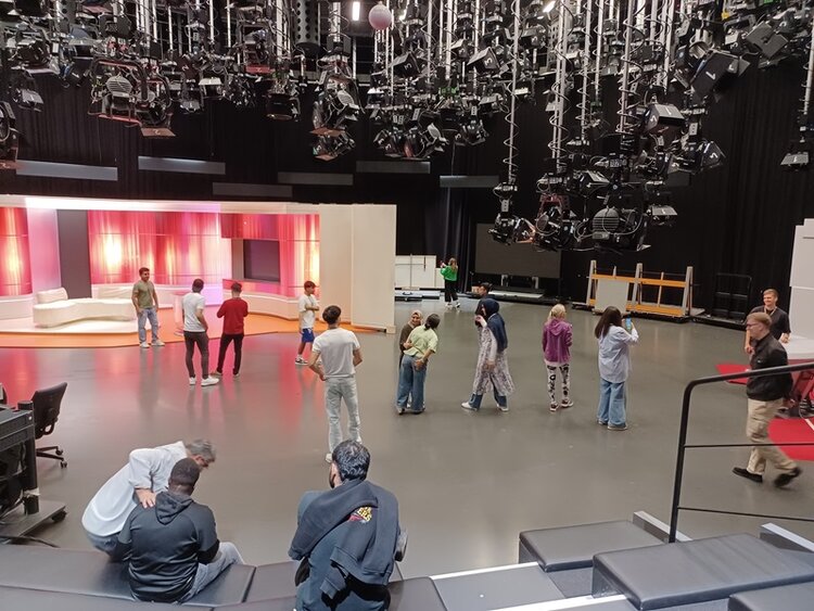 Berufssprachkurs besucht Fernsehsender Teilnehmende der Euro-Schulen Mainz sehen sich in einem großen Fernsehstudio um, an der Decke hängen unzählige Scheinwerfer, die Kulisse einer Fernsehsendung ist zu sehen.
