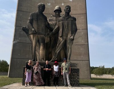 Teilnehmende stehen vor der überlebensgroßen Skulpturengruppe, die den Titel "Befreiung" trägt und vom Bildhauer René Graetz stammt.
