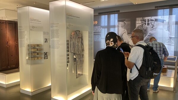 Ausflug zur Gedenkstätte Sachsenhausen Teilnehmende stehen in der Gedenkstätte Sachsenhausen und betrachten Exponate, darunter gestreifte KZ-Häftlingskleidung.