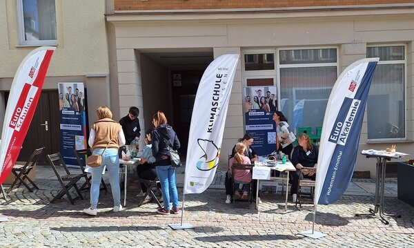 Mit Herz und Kreativität dabei Menschen informieren sich am Stand der Euro Akademie und der Euro-Schulen Hohenstein-Ernstthal beim Frühlingsfest „HOT im Herzen“. Aufsteller und Banner zeigen das Bildungsangebot, während Kinder und Erwachsene an Tischen basteln.