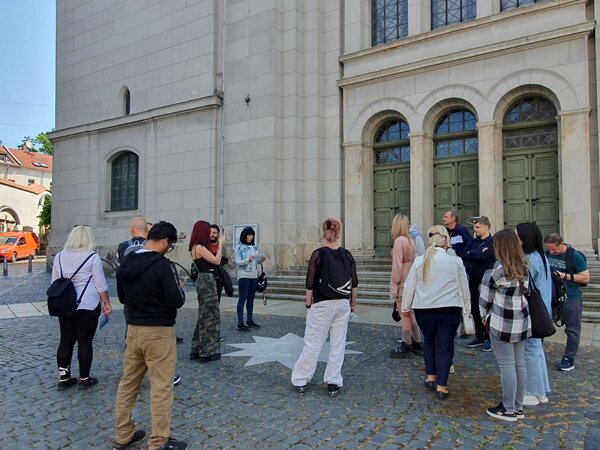 Auf den Spuren der Geschichte Zittaus Eine Gruppe von Menschen steht vor einem historischen Gebäude mit großen, grünen Doppeltüren und hohen Fenstern. Die Gruppe scheint sich auf eine Führung oder Besichtigung vorzubereiten.