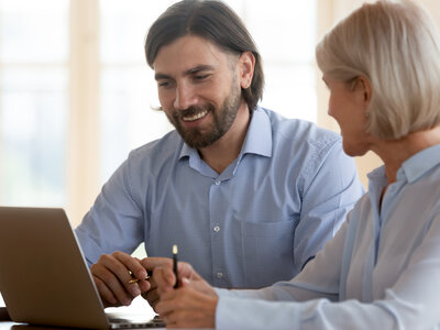 Ein Mann und eine Frau sitzen vor einem Laptop und unterhalten sich.