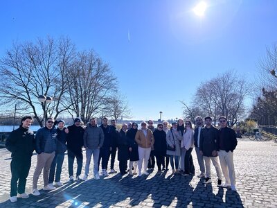 Gruppenbild Die Teilnehmenden des Orientierungskurses posieren bei strahlendem Sonnenschein am Rheinufer für ein Gruppenbild.