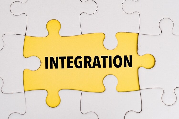 Solingen – Eine Stadt mit Perspektive für Geflüchtete Verschiedene weiße Puzzleteile sind zusammengesetzt und in der Mitte sind zwei dieser Teile orange gefärbt. Auf diesen Teilen steht "Integration" in Schwarz.