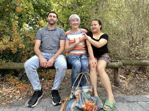 Abschluss des Deutschkurses Zwei Teilnehmende sitzen mit ihrer Dozentin auf einem Holzbalken und posieren für ein Abschiedsfoto.