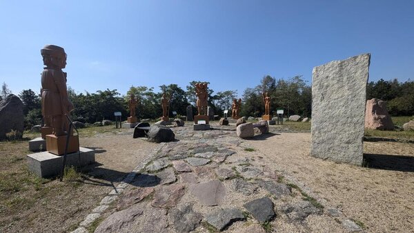 Abschlussfahrt: Erlebnispark Teichland Zwischen Steinblöcken stehen überlebensgroße Holzfiguren auf einem Platz, der teilweise mit großen Steinen gepflastert ist. Im Hintergrund stehen Bäume.