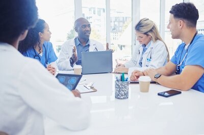 Ein Arzt sitzt mit seinen Kolleg*innen aus der Pflege vor einem aufgeklappten Laptop und bespricht sich mit dem interkulturellen Team. 