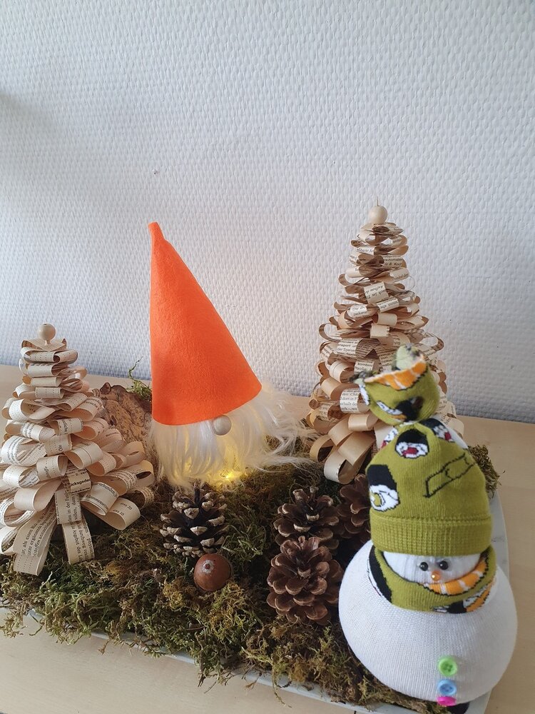 Bald ist Zwischenprüfung! Auf dem Foto tummeln sich in einem weihnachtlichen Gesteck auf der Basis von echtem Moos ein Wichtel mit orangefarbener Filzmütze und ein Schneemann, der aus zwei verschiedenen Socken hergestellt wurde. Außerdem stehen auf dem Gesteck neben echten Tannenzapfen noch zwei Weihnachtsbäume aus Buchseitenschnipseln.
