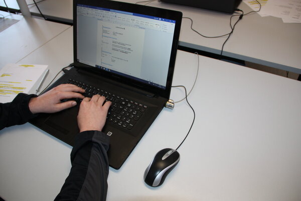 Wöchentliches Bewerbungstraining mit Jobcoach Frau Sacher Zwei Hände auf der Tastatur eines Laptops, auf dessen Monitor ein geöffnetes Dokument zu sehen ist. An den Laptop ist eine Maus angeschlossen.