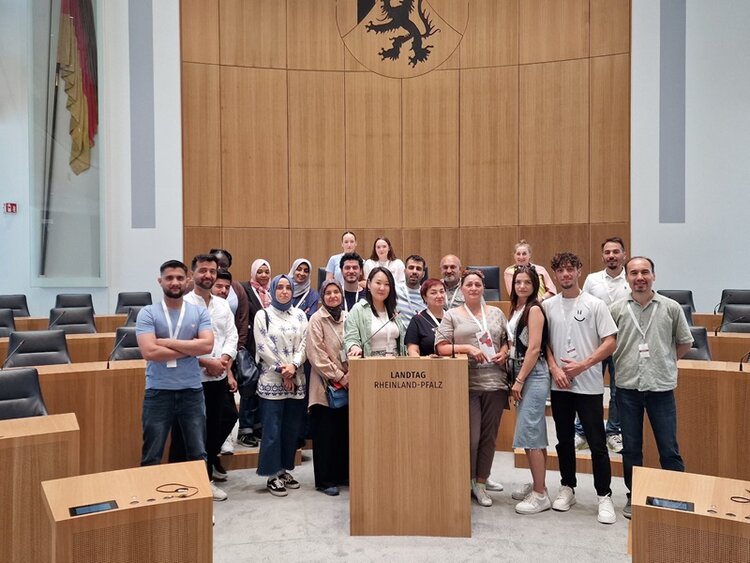 Integrationskurs besucht den Landtag Rheinland-Pfalz Die weiblichen und männlichen Teilnehmenden des Integrationskurses der Euro-Schulen Mainz stehen gemeinsam hinter dem Rednerpult des Landtages und posieren für ein Gruppenfoto.