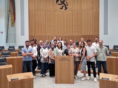 Die weiblichen und männlichen Teilnehmenden des Integrationskurses der Euro-Schulen Mainz stehen gemeinsam hinter dem Rednerpult des Landtages und posieren für ein Gruppenfoto.