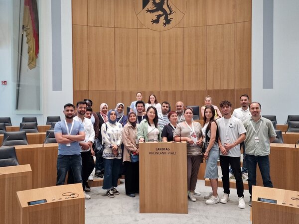 Integrationskurs besucht den Landtag Rheinland-Pfalz Die weiblichen und männlichen Teilnehmenden des Integrationskurses der Euro-Schulen Mainz stehen gemeinsam hinter dem Rednerpult des Landtages und posieren für ein Gruppenfoto.
