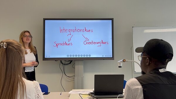 Mit KI zu barrierefreier Bildung – Teil 1 Videodreh an den Euro-Schulen Leipzig. Eine Mitarbeiterin steht vorn an einem Bildschirm und erklärt etwas.