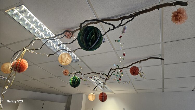 Kulinarischer Karneval-Auftakt An einer Decke aus Spanplatten hängen zwei Äste, an denen verschiedenen Dekogegenstände angebracht sind.