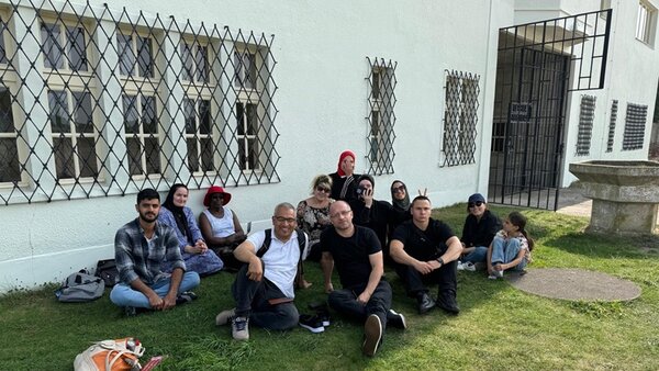 Ausflug zur Gedenkstätte Sachsenhausen Die Teilnehmenden und ihr Lehrer posieren sitzend vor der Gedänkstätte Sachsenhausen für ein Gruppenfoto.
