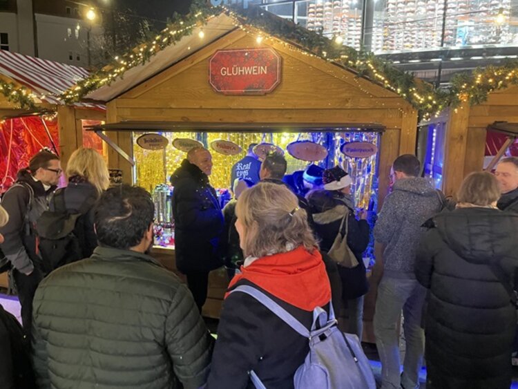 Weihnachtsfeier in Berlin Mtarbeitende stehen vor einem Glühweinstand auf dem Weihnachtsmarkt.
