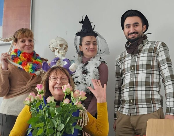 Faschingsdienstag an der Euro Akademie und den Euro-Schulen Dresden, Meißen und Riesa Vier Personen in festlichen Verkleidungen posieren in einem Raum. Eine Frau mit Blumenkranz und einem Skelettkopf in der Hand, eine andere mit Hexenhut und Federboa, ein Mann mit einem Halstuch sowie eine ältere Dame mit violetten Plüsch-Ohren und einem Strauß rosa Rosen. Alle lachen fröhlich in die Kamera.