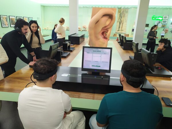Sonniger Exkursionstag der Euro-Schulen Dresden: Spannende Einblicke in Wissenschaft und Kultur Zwei Personen tragen Kopfhörer und interagieren mit einer audiovisuellen Station in einem Museum. Im Hintergrund sind große Modelle von Ohren und andere anatomische Darstellungen zu sehen.