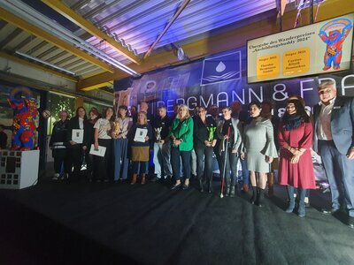 Ein Gruppenfoto von Rednern, Preisträgern und Verantwortlichen auf einer Bühne mit blauem Hintergrund.