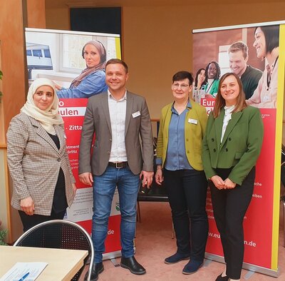 Gruppenfoto Vier Teilnehmende stehen vor großen Euro-Schulen Roll-Ups im Hintergrund und posieren gemeinsam für ein Gruppenfoto.