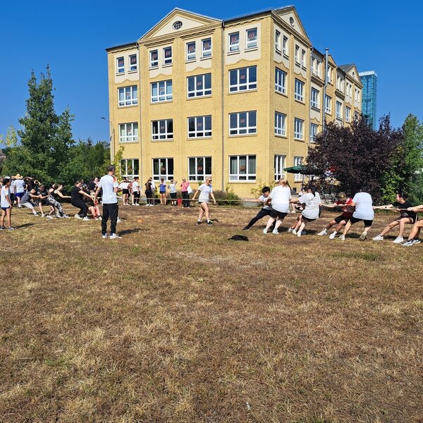 Sportfest – mal anders Vor dem Schulgebäude treten auf einer Wiese zwei Teams im Tauziehen gegeneinander an.