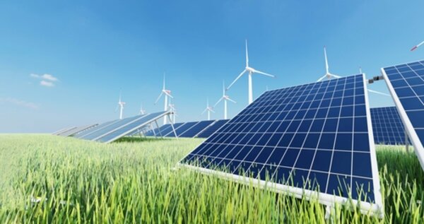 Schritt für Schritt grüner: Die Euro-Schulen setzen auf Ökostrom! Solarzellen stehen in einem Feld mit grünen Gräsern, dahinter erkennt man mehrere moderne Windräder. Der blaue Himmel ist fast wolkenlos.