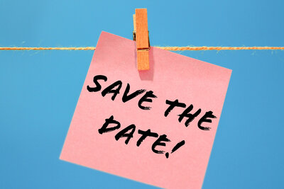 Hinweis auf einen Termin Die Aufschrift "Save the Date!" steht wie handschriftlich geschrieben auf einem rosafarbenen Notizzettel, der mit einer Holzwäscheklammer an eine Kordel gehängt ist. Der Hintergrund ist blau.