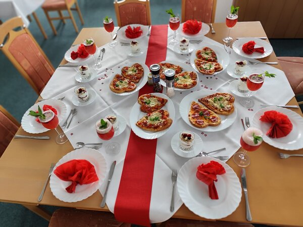 Praxisnahe Berufsorientierung: BRAFO im Strukturelement I Eine Nahaufnahme des gedeckten Tisches mit herzförmigen Pizzen, Gläsern mit roten Getränken und kleinen Desserts in Gläsern. Der Tisch ist mit roten Servietten und einer roten Tischdecke dekoriert.
