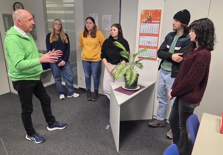Spende an das Kinder- und Jugendhospiz Herr Köhler vom Hospiz berichtet interessierten Auszubildenden und Teilnehmenden, die gemeinsam mit ihm im Raum stehen, von der Arbeit im Hospiz.