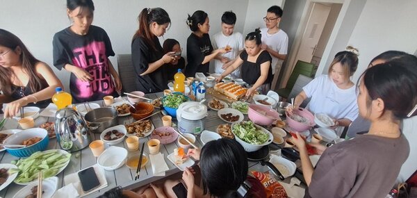 Abschluss des Deutschkurses Letzte Vorbereitungen der Teilnehmenden, die ihre Gerichte auf der langen eingedeckten Tafel platzieren.