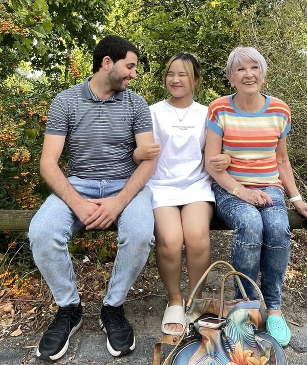 Abschluss des Deutschkurses Zwei Teilnehmende sitzen mit ihrer Dozentin auf einem Holzbalken und posieren für ein Abschiedsfoto.