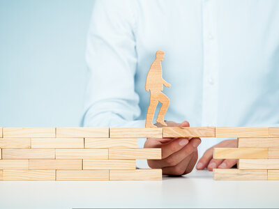 Eine Person baut mit Holzbausteinen eine Brücke, über die eine Holzfigur läuft.