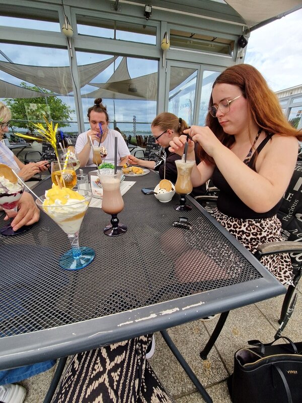 Die Auszubildenden sitzen draußen in einem Eiscafé und genießen ihre großen, bunten Eisbecher.