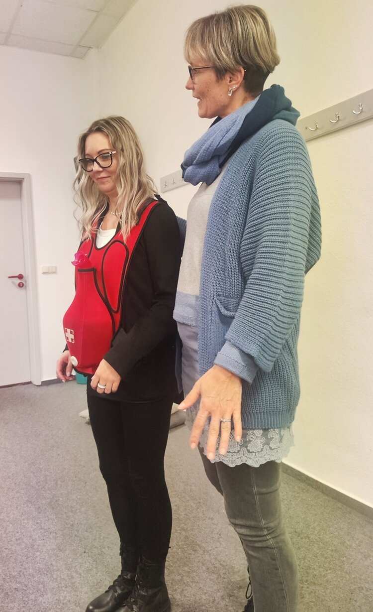 Helfen können alle lernen Mitarbeitende und Kursleiterin beim Erste Hilfe Kurs, die eine Übung erklärt.