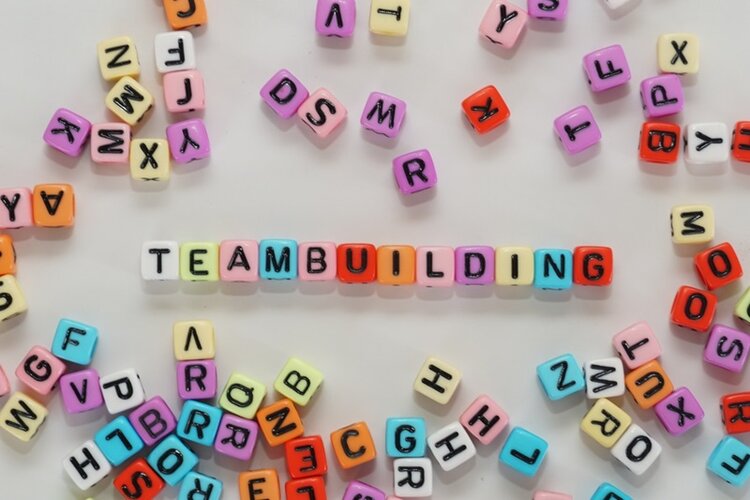 Viele bunte Buchstabenwürfel liegen auf weißem Untergrund, das Wort Teambuilding liegt in der Mitte.