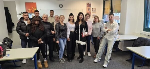 Weihnachtsfeiern in Köln Die Kursteilnehmenden stehen vor einer Tafel in ihrem Klassenzimmer und lächeln in die Kamera.
