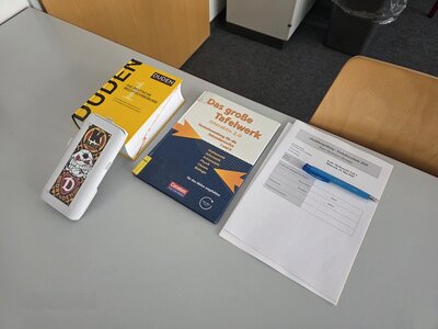 Auf einem weißen Tisch liegt ein Deutsch-Duden, ein Kugelschreiber, Arbeitsblätter zut Prüfung sowie ein Lehrbuch.
