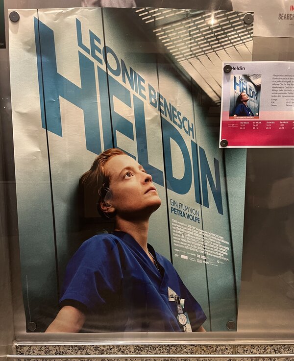 Abwechslung im Schulalltag: ein Kinobesuch Das Plakat zum Film "Heldin". Zu sehen ist eine Pflegerin in blauer Arbeitskleidung, die erschöpft an einer Aufzugwand lehnt und mit leerem Blick nach oben sieht. Über ihr in baluer Schrift: Leonie Benesch – Heldin