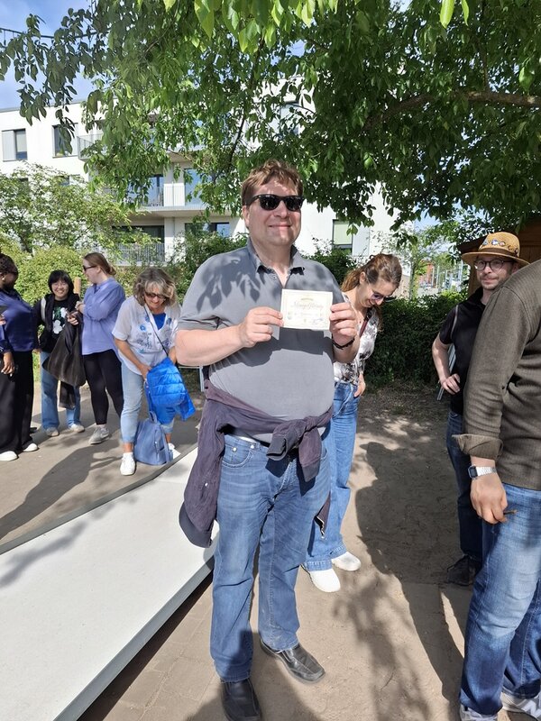 Teamtag der Euro-Schulen Berlin Brandenburg Herr Daske trägt eine dunkle Sonnenbrille und zeigt stolz seine Siegerurkunde im Minigolf in die Kamera.