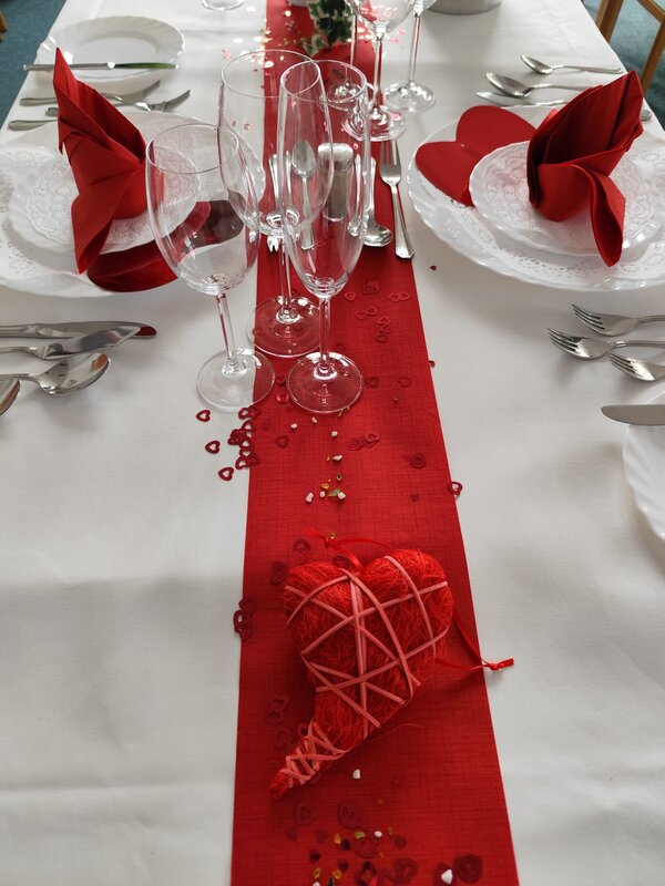 Praxisnahe Berufsorientierung: BRAFO im Strukturelement I Eine stilvolle Tischdekoration mit einem roten Läufer, roten Servietten und transparenten Weingläsern. In der Mitte liegt ein dekoratives, geflochtenes rotes Herz.