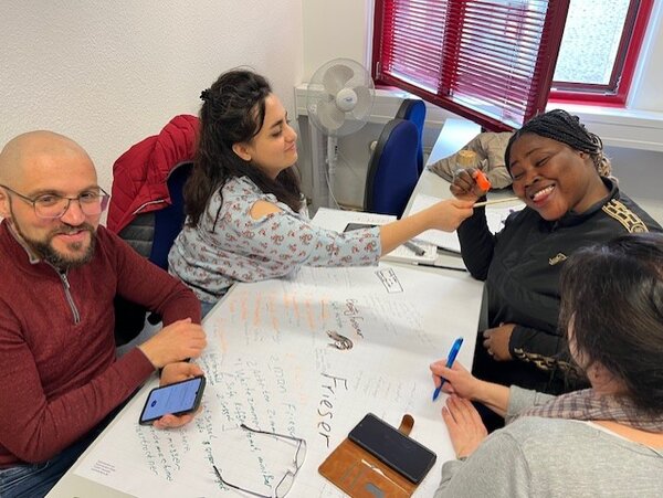 Erfolgreiche Gruppenarbeit im Berufssprachkurs Ein Mann und drei Frauen gestalten gemeinsam ein Plakat.