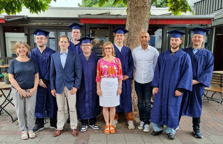 Gelungene Zeugnisfeier an der Euro Akademie Gruppenbild der Absolvent*innen in einem Biergarten unter großen Bäumen. Ein Teil der Personen ist in dunkelblaue Talare gehüllt und trägt Absolventenhüte.