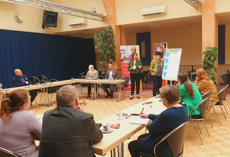 Gelungene Auftaktberatung der Arbeitsmarktmentoren Teilnehmende sitzen an Tischen in U-Form und schauen nach vorn zu zwei Teilnehmenden, die an einem Flipchart präsentieren.